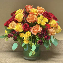 Mixed roses in red, yellow, and peach arranged in a glass vase
