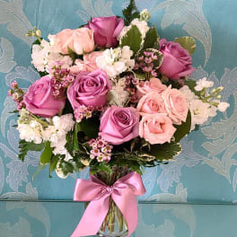 Bouquet of pink and lavender roses in a clear glass vase with a pink ribbon