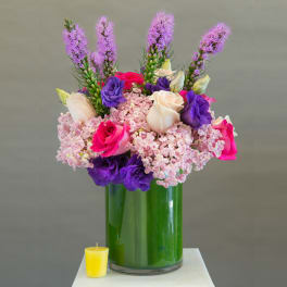 Pink, purple, and cream roses in a tall glass vase with a small yellow candle nearby