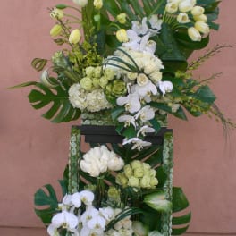 Tall floral arrangement with white orchids, roses, and tropical leaves