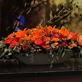 Long orange floral arrangement with roses and lilies in a low container
