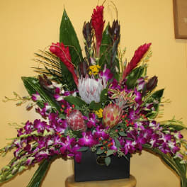 Large tropical flower arrangement in a black container with purple orchids and red blooms