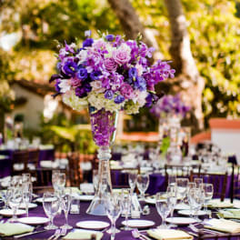 Purple floral centerpiece in a tall glass vase on a banquet table