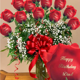 Red roses in a glass vase with a birthday ribbon and card
