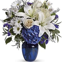 White lilies and daisies with blue hydrangea in a blue vase