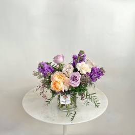 Mixed bouquet of pastel roses and purple flowers in a glass vase