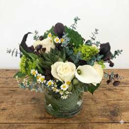 White roses and calla lilies in a glass vase with greenery