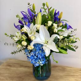 White lilies and blue hydrangeas in a glass vase with purple iris
