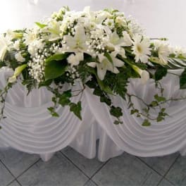White floral arrangement with lilies and daisies on a draped table