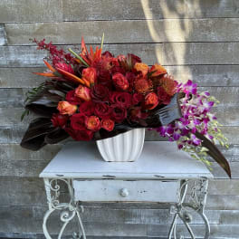 Large red and orange floral arrangement in a white vase with purple orchids