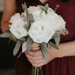 White rose bouquet with eucalyptus held by a person in a burgundy dress