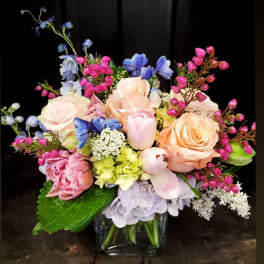 Pastel bouquet of roses, tulips, hydrangea, and blue flowers in a glass vase