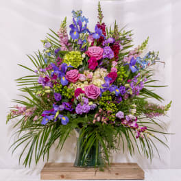 Large mixed bouquet of purple, pink, and blue flowers in a glass vase