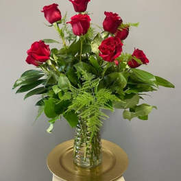 Red roses arranged in a clear glass vase with greenery