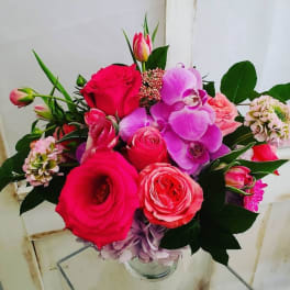 Bouquet of pink roses, orchids, and tulips in a glass vase