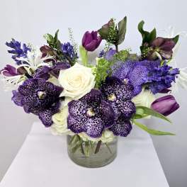 Purple and white floral arrangement in a clear glass vase