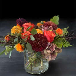 Mixed bouquet of orange, burgundy, and pink flowers in a clear glass vase