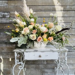 Large pastel floral arrangement in a white bowl on a decorative table