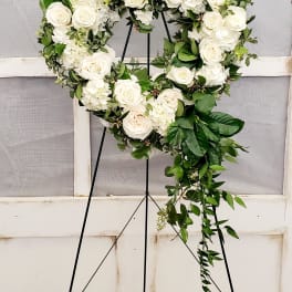 Heart-shaped white rose wreath on a black stand with trailing greenery