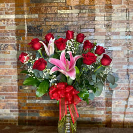 Red roses and pink lilies in a glass vase with a red ribbon