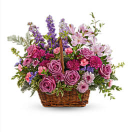 Basket arrangement of purple and pink flowers with a wicker handle