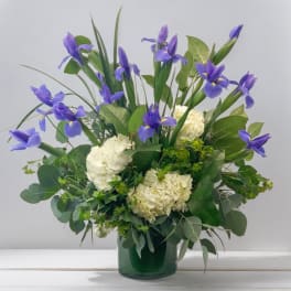 Purple iris and white hydrangea arrangement in a green glass vase