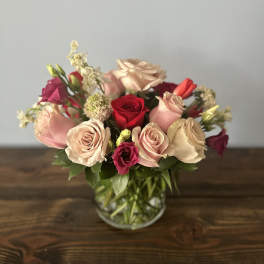 Low bouquet of blush pink and red roses with accent blooms in a clear glass vase