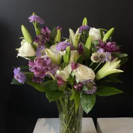 Bouquet of white lilies, roses, and purple flowers in a glass vase