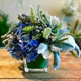 Blue and green floral arrangement in a square glass vase