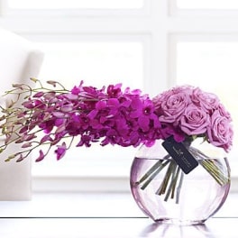 Purple orchid and lavender rose arrangement in a round glass vase