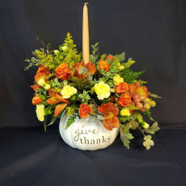 Orange and yellow floral arrangement in a white pumpkin container with a candle