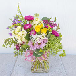 Mixed bouquet of pink, yellow, white, and purple flowers in a glass vase