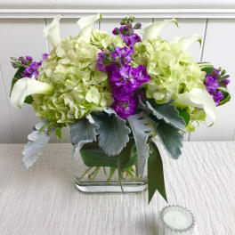 Arrangement of green hydrangeas, purple stock, and white calla lilies in a glass vase