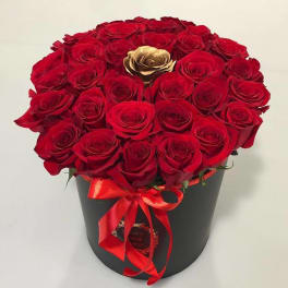 Red roses arranged in a black hatbox with a red ribbon
