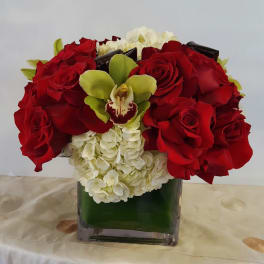 Red roses and white hydrangeas arranged in a square glass vase with a green orchid