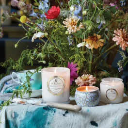 Wildflower arrangement with three lit candles and a turquoise cup on a painted cloth