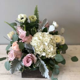 Low arrangement of white hydrangea, pale pink roses, and white blooms in a wooden box.