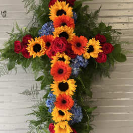 Cross-shaped floral arrangement with sunflowers, gerbera daisies, roses, and blue hydrangeas