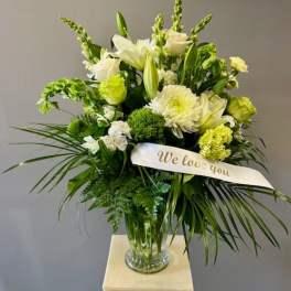 White and green sympathy arrangement in a glass vase with a "We love you" ribbon