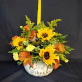 Sunflower and orange floral arrangement in a white vase with a tall yellow candle