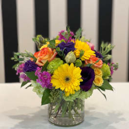 Mixed bouquet in a clear glass vase with yellow, purple, pink, and orange blooms