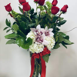 Red roses and pale orchids in a clear glass vase with a red ribbon