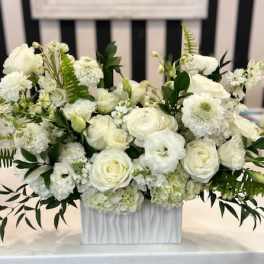 Low white flower arrangement with roses and mixed blooms in a rectangular white vase