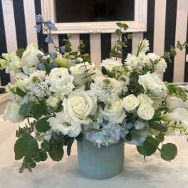 White roses and calla lilies in a pale blue vase with blue accents