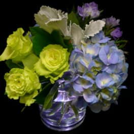 Compact arrangement of green roses and blue hydrangeas in a clear glass vase on a black background.