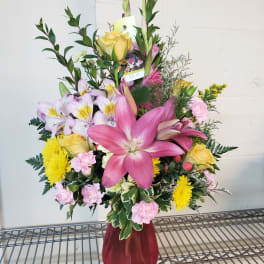 Mixed bouquet with pink lilies, yellow roses, and pink carnations in a burgundy vase