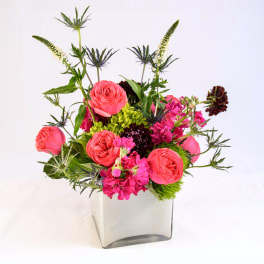 Pink roses and magenta flowers in a clear square vase