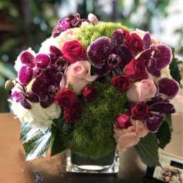 Bouquet of pink and red roses with purple orchids in a glass vase