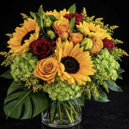 Bouquet of sunflowers, roses, and hydrangeas in a glass vase
