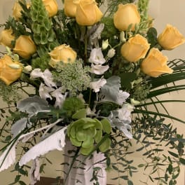 Yellow roses and white flowers in a tall arrangement with cascading greenery